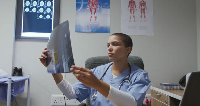 Doctor wearing scrubs and stethoscope examining x-ray in a clinic. This image is ideal for use in healthcare services promotions, medical practice websites, patient information brochures, and educational materials for medical students.