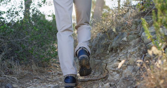 Caucasian man hikes on a rocky trail outdoors. Sturdy boots grip the terrain, suggesting an adventurous spirit.