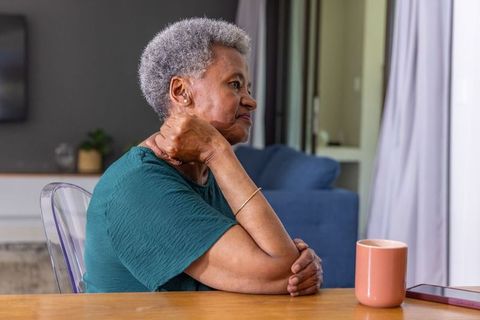 Senior african american woman reflecting while touching neck near mug and phone