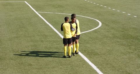 Soccer Players Strategizing on Field in Yellow Jerseys