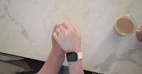 Senior couple holding hands with smartwatch and coffee on marble countertop