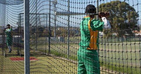 Batsman practicing in outdoor cricket nets wearing green and yellow uniform and helmet