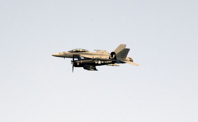 This image shows an F/A-18 Super Hornet jet flying in formation with a World War II Vought F4U Corsair during an air show at the Kennedy Space Center Visitor Complex in Florida. It juxtaposes modern and historical aviation, reflecting advancements in military aircraft technology. Suitable for content on aviation history, military performances, aerospace events, and NASA activities.