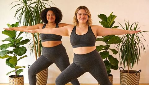 Plus-size women practicing partner yoga in matching gray activewear with indoor plants
