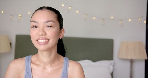Young Woman Relaxing in Cozy Bedroom with Gentle Smile