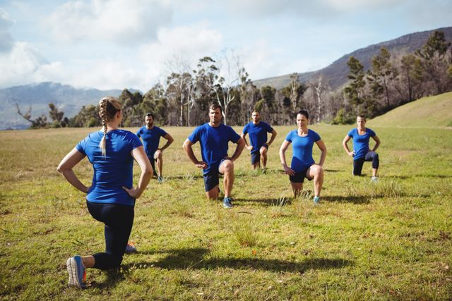 Group of diverse participants receiving guidance from female trainer during boot camp session in natural outdoor setting. Ideal for illustrating teamwork, outdoor fitness, coaching, and health-oriented activities. Useful for fitness blogs, promotional material for workout programs, or motivational content focused on active lifestyles.