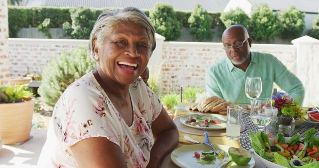 Happy senior couple enjoys a meal outdoors on a sunny day. This image is great for promoting healthy lifestyles, retirement living, and family gatherings.