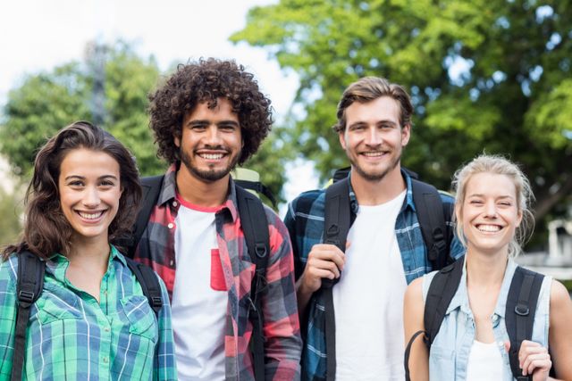 Group of friends standing together and smiling at camera outdoors. Ideal for use in advertisements, social media posts, and articles about friendship, youth, outdoor activities, and casual lifestyle.