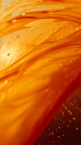 Backlit amber syrup forming flowing ribbons and droplets in macro vertical slow-motion video