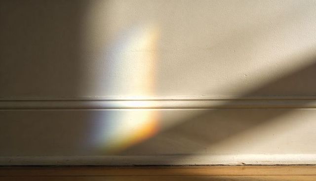 Sunlight casting colorful prism on interior wall with diagonal shadow and baseboard