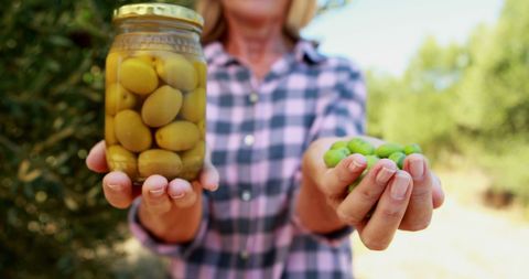 Woman Holding Jar of Preserved and Fresh Olives on Farm