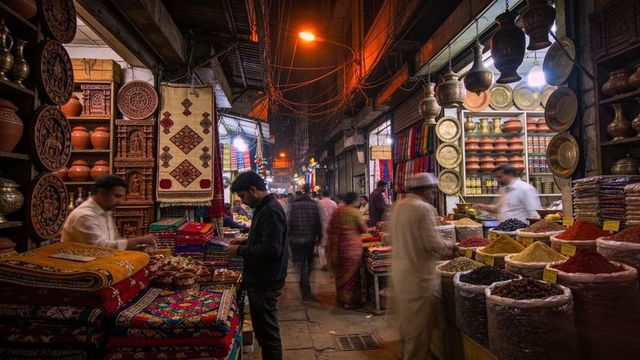 Browsing indian bazaar alley: man inspecting colorful textiles, spice sacks, pottery