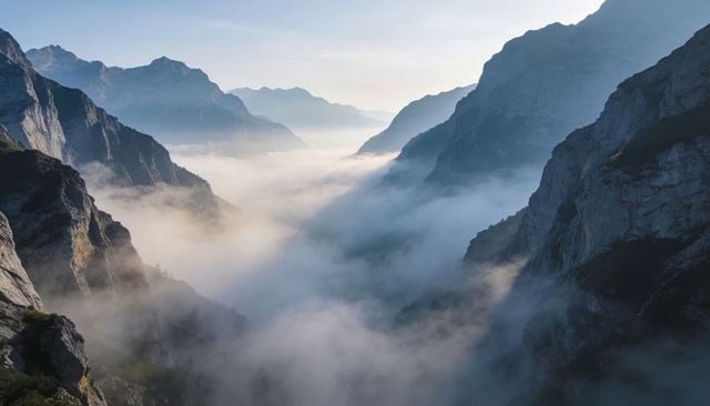 Fog shrouding alpine valley at dawn between rugged cliffs and distant peaks