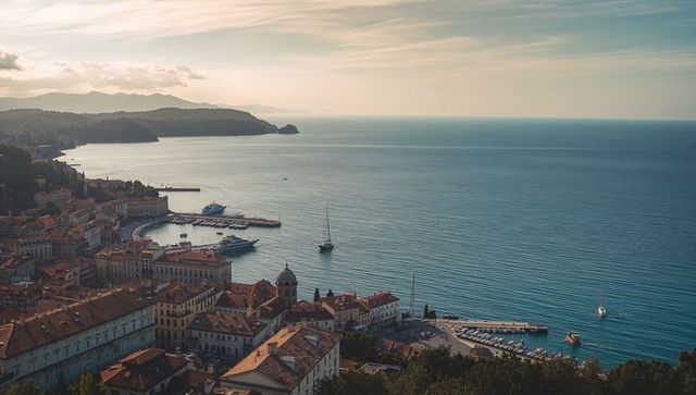 Panoramic coastal town overlooking marina with red-tiled roofs and sailboats at golden hour