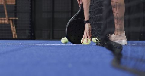 Female Athlete Picking Up Padel Balls on Blue Court with Racket