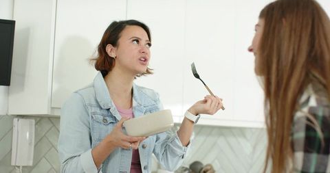 Women Talking in Bright Kitchen Holding Ceramic Bowl and Fork Showing Smartwatch