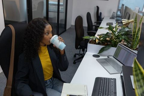African american professional sipping reusable cup while working at modern office desk