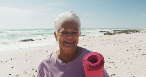 Senior Woman on Beach Holding Yoga Mat Smiling