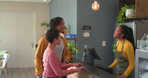 Couple chatting with barista at cozy cafe counter with warm lighting, wood decor and plants