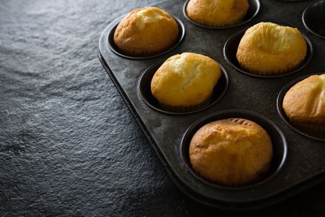 Freshly baked plain cupcakes in a baking tray. Ideal for use in food blogs, recipe websites, cooking magazines, and bakery advertisements. Perfect for illustrating homemade baking, dessert preparation, and kitchen activities.