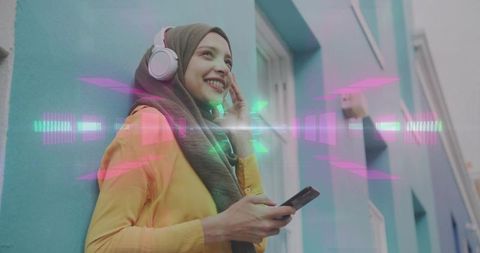Young woman wearing hijab listening to music with headphones, smartphone, neon waveform