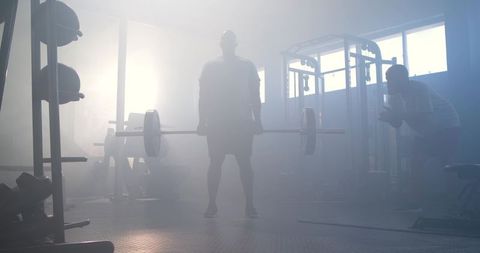 Silhouetted athlete deadlifting heavy barbell in foggy backlit gym for strength training