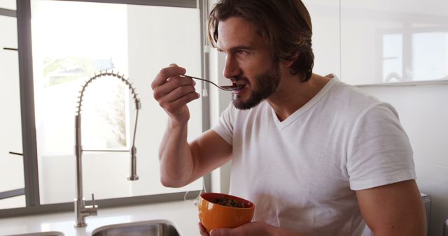 Cheerful man enjoying healthy breakfast in modern kitchen. Perfect for lifestyle blogs, healthy eating campaigns, and kitchen appliance advertisements. Depicts positive and healthy morning routine.
