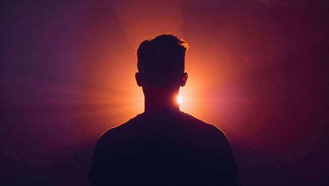Silhouetted man standing against intense orange backlight with halo and lens flare