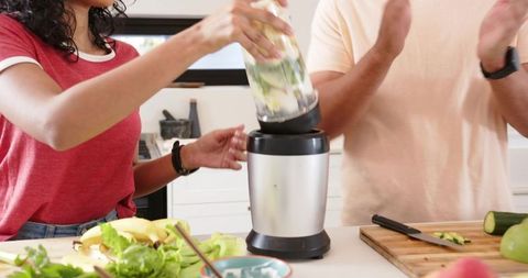 Couple preparing green smoothie using personal blender on bright modern kitchen counter