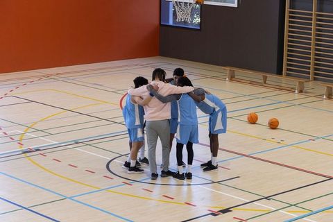 Diverse basketball team huddling indoors in gym with coach