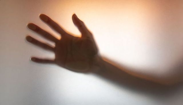Reaching hand casting soft shadow and translucent silhouette on frosted glass panel with warm light