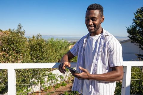 Man enjoying leisure time on balcony with smartphone in sunny weather