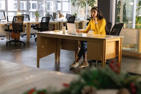 Indian woman in yellow top working on laptop in modern open-plan coworking office with coffee