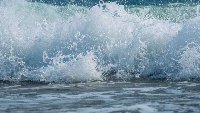 Teal surf crashing onto sandy shallow shoreline with white foam and sea spray