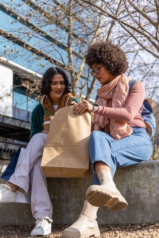 Young friends sharing takeout and coffee while sitting on urban ledge with backpacks