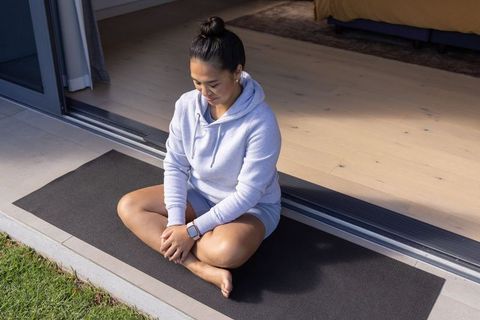 Asian woman practicing mindfulness on yoga mat at home threshold in hoodie and shorts