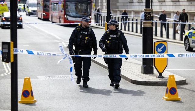 Two uniformed police officers walking patrol behind cordoned urban street with police tape