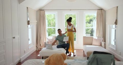 Couple discussing documents using laptop in sunlit living room