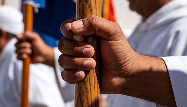 Gripping hand on polished wooden staff during ceremonial procession in bright sunlight