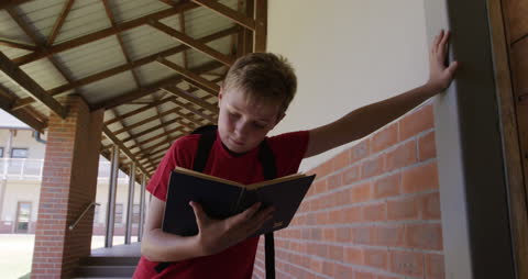 Boy Reading Book in School Corridor