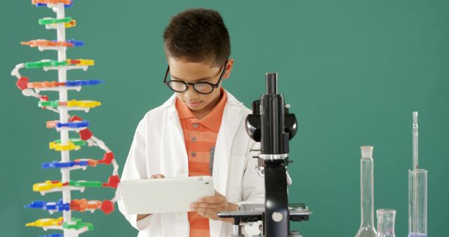Young boy wearing glasses and a lab coat focusing on a tablet with various laboratory equipment around him, including a microscope and test tubes. Perfect for educational materials, science-themed websites, and promotional content for STEM programs for children.