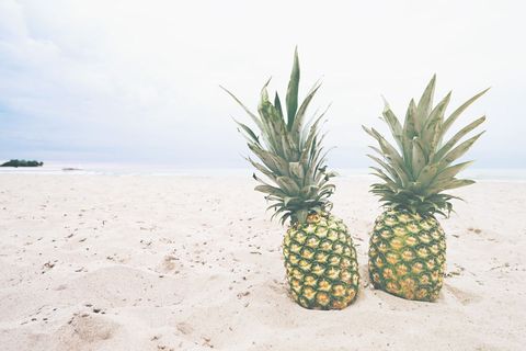 Two Pineapples on White Sandy Beach Creating Tropical Vacation Mood and Summer Vibes