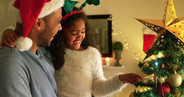 Biracial couple enjoys decorating a Christmas tree at home. They share a warm moment in the festive spirit, surrounded by holiday lights.