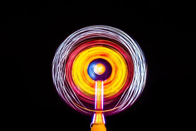 Capturing colorful motion blur of a spinning wind fan on black background, creating an abstract and celebratory effect. Perfect for illustrating concepts of motion, energy, spirit of festivals, and amusement park attractions. Can be used in designs for nightlife events, posters, technology, or artistic projects focusing on light and motion.