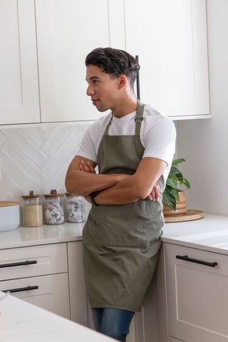 African american man leaning on counter wearing olive apron in modern minimalist kitchen