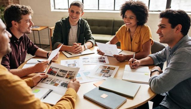 Creative design team collaborating over printed layouts around round table in office