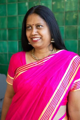Senior indian woman in pink saree smiling by green tiles