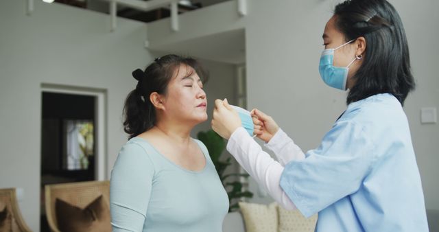 This image depicts an attentive healthcare worker assisting a woman in putting on a face mask indoors, emphasizing the importance of health and safety measures. This can be used in articles, brochures, or websites related to healthcare services, wellness guidance, pandemic safety protocols, or medical assistance.
