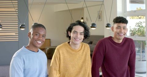 Diverse young men smiling together in modern living room wearing knit sweaters