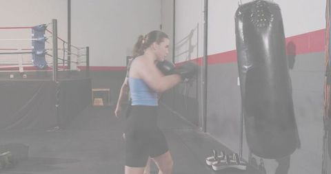 Female boxer punching heavy bag during intense boxing training session in gym showing focus
